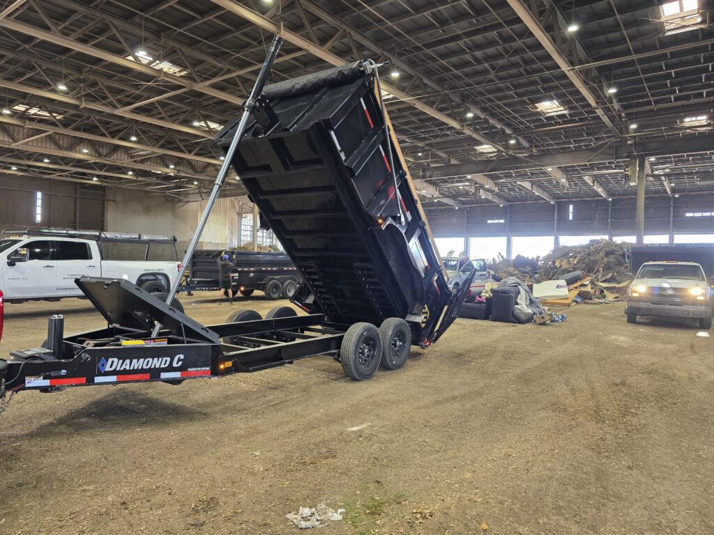 A dump trailer with a raised bed is unloading materials in a large indoor space