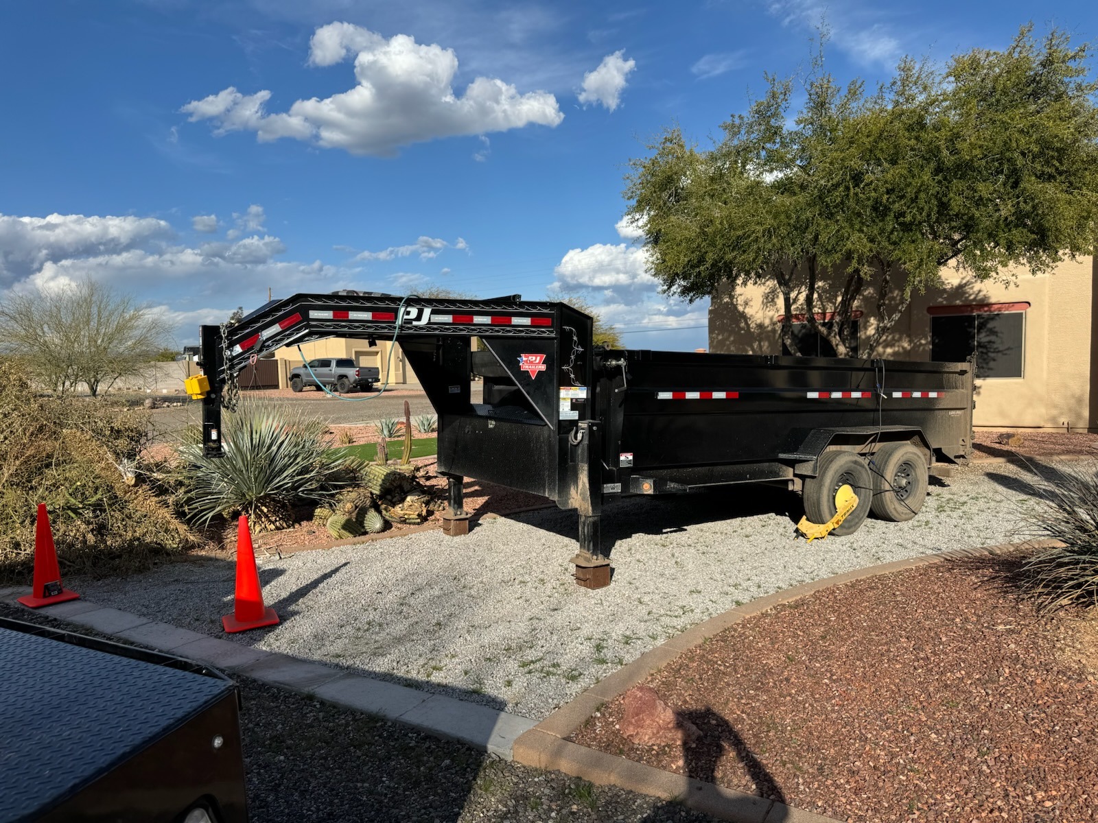 Black dump trailer parked on gravel, with safety cones nearby